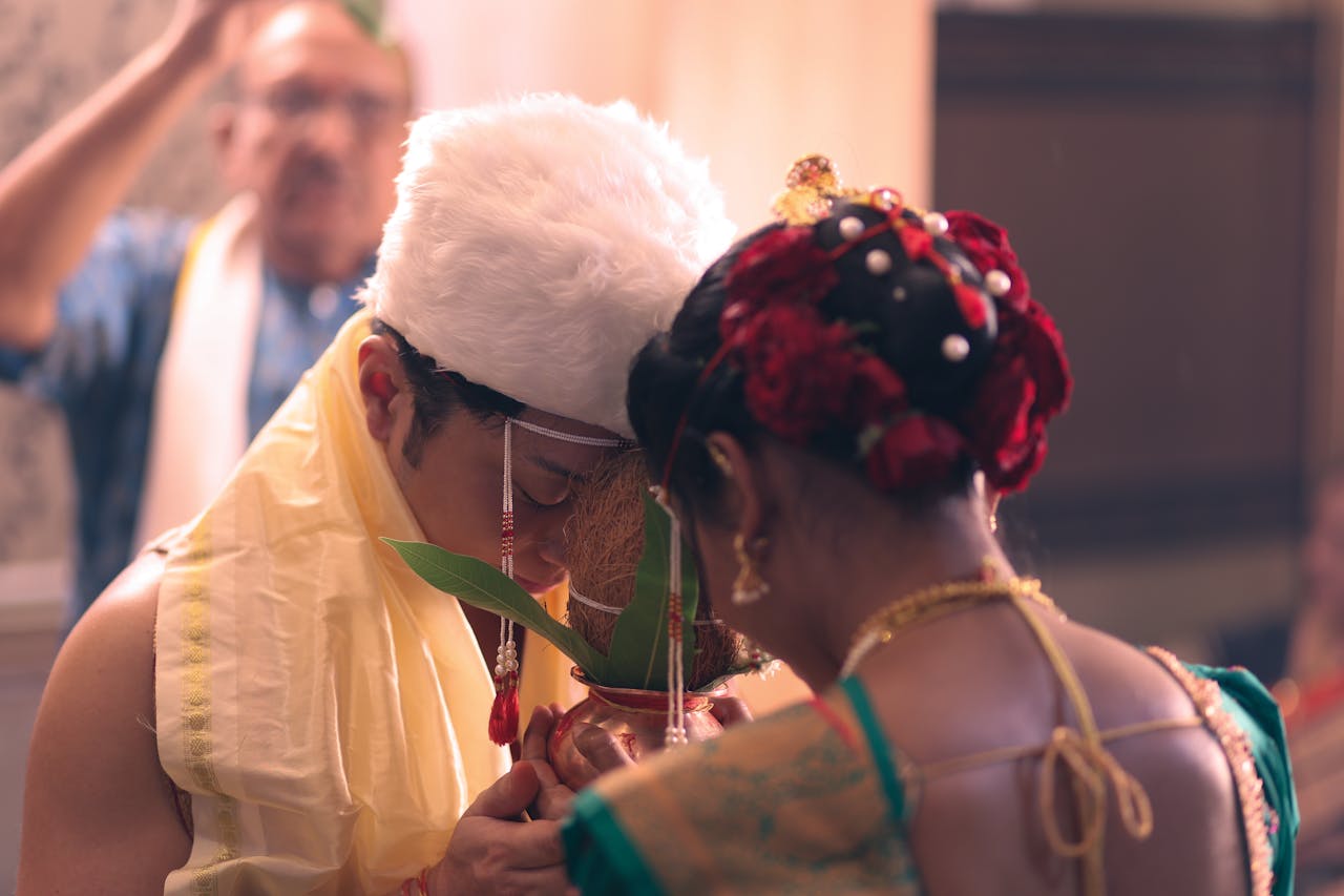A couple performing a traditional Indian wedding ritual indoors, captured with cultural and festive elements.